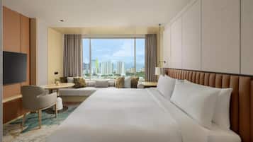 A hotel room with a large bed, a desk, a chair, a TV, and a view of the cityscape.