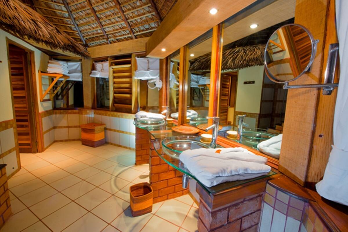 A bathroom with a glass sink, wooden accents, and a thatched ceiling.