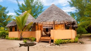 A thatched-roof bungalow with a wooden exterior, a staircase leading to the entrance, and a signpost with room numbers. - Nosy Saba Private Island & Spa (Nosy Saba)