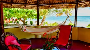 A room with a hammock, two red chairs, a glass table, and a view of the beach and ocean. - Nosy Saba Private Island & Spa (Nosy Saba)