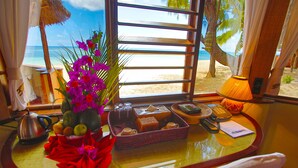 A table with a vase of flowers, a fruit bowl, a tray of toiletries, and a view of the beach. - Nosy Saba Private Island & Spa (Nosy Saba)
