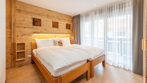 A modern bedroom with a wooden headboard, a large bed with white linens, a bedside table, and a nightstand. - Haus Colosseo by Zermatt Premium Apartments (Zermatt)