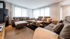 A modern living room with a fireplace, two sofas, a coffee table, and a large window with sheer curtains. - Haus Colosseo by Zermatt Premium Apartments (Zermatt)