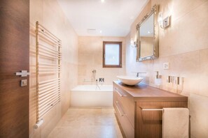 Un baño moderno con un tocador de madera, un espejo grande y una bañera independiente.
