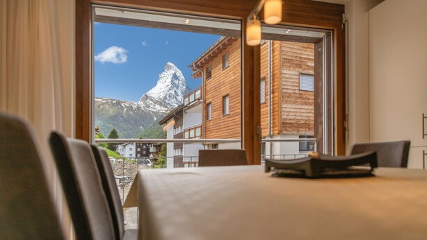 A hotel room with a large window offering a view of a mountain and buildings. - Haus Colosseo by Zermatt Premium Apartments (Zermatt)