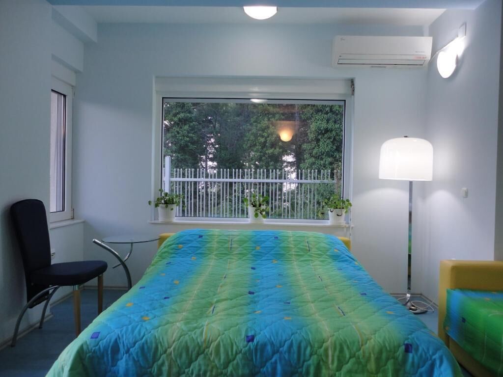 Quarto com uma cama, uma cadeira, uma janela com vista para árvores e um abajur.