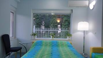 Quarto com uma cama, uma cadeira, uma janela com vista para árvores e um abajur.
