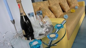 A room with a yellow sofa, a glass table with decorative items, and a bottle of champagne. - Accommodation J&T (Ohrid)