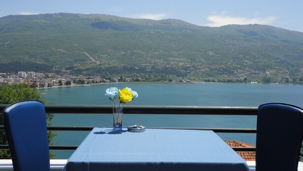 A table with a vase of flowers and a plate, overlooking a lake with a mountain in the background. - Accommodation J&T (Ohrid)
