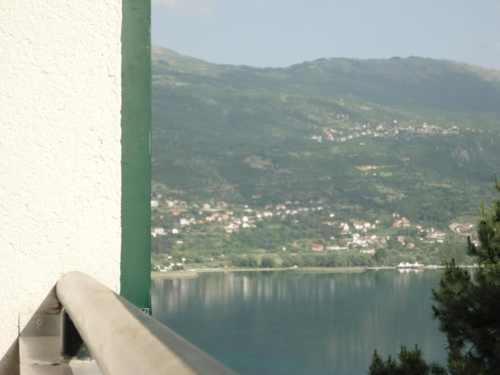 Vista de un lago con un pueblo al fondo y una barandilla verde en primer plano.