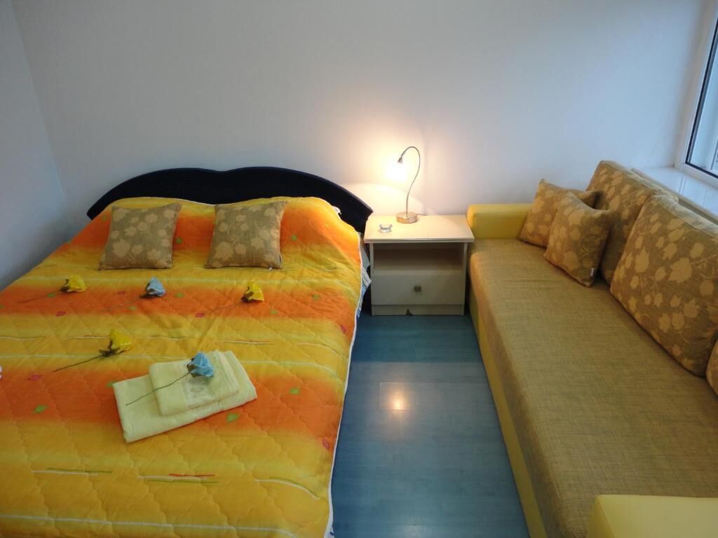 A bedroom with a bed, a nightstand with a lamp, a sofa, and a window.