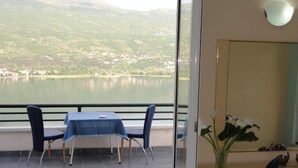 A balcony with a table and chairs, a vase with flowers, and a view of a lake and mountains. - Accommodation J&T (Ohrid)