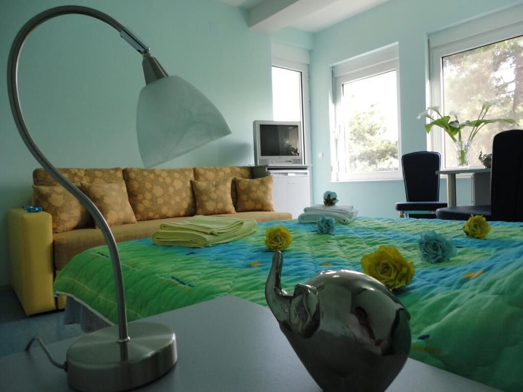 Ein Schlafzimmer mit einem Bett, einem Schreibtisch mit Lampe, einem Fernseher und einem Fenster mit Blick auf Bäume.