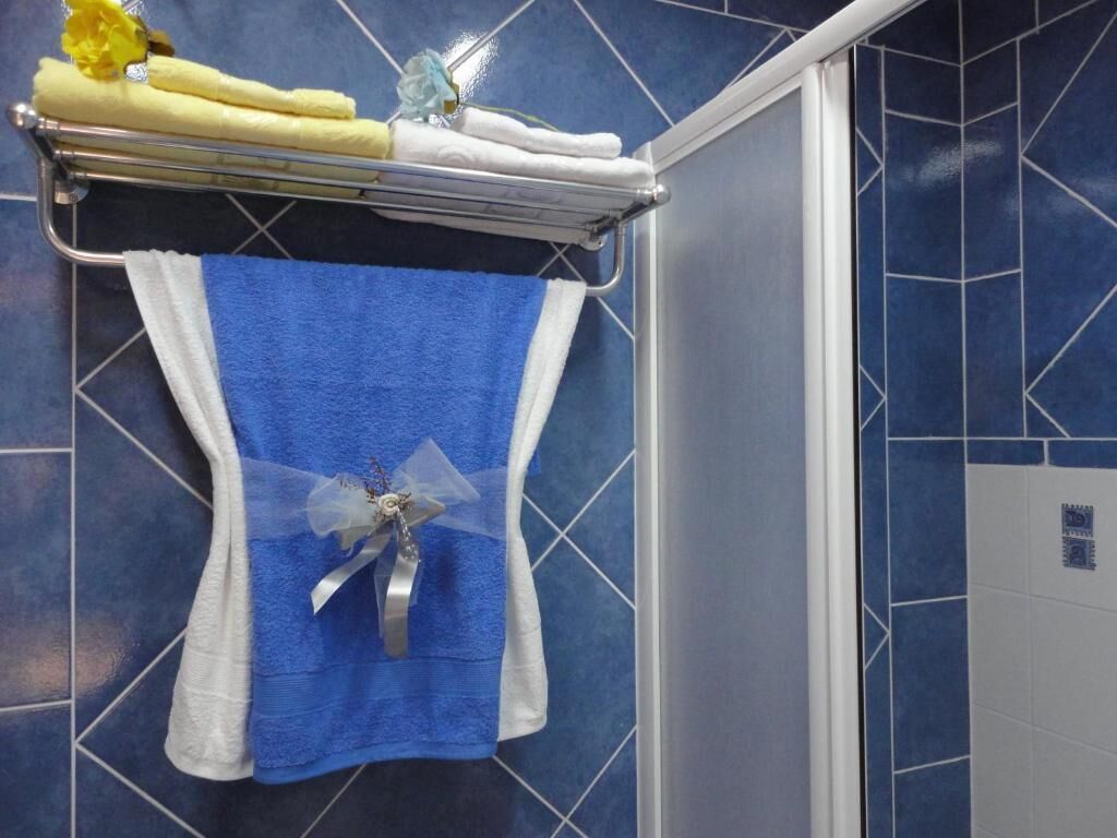 A bathroom with a blue tiled wall, a towel rack with folded towels, and a blue towel with a decorative bow.