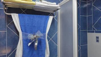 A bathroom with a blue tiled wall, a towel rack with folded towels, and a blue towel with a decorative bow.