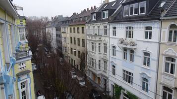 Une rangée d’immeubles à plusieurs étages, dotés de balcons, avec des voitures garées et une rue étroite.