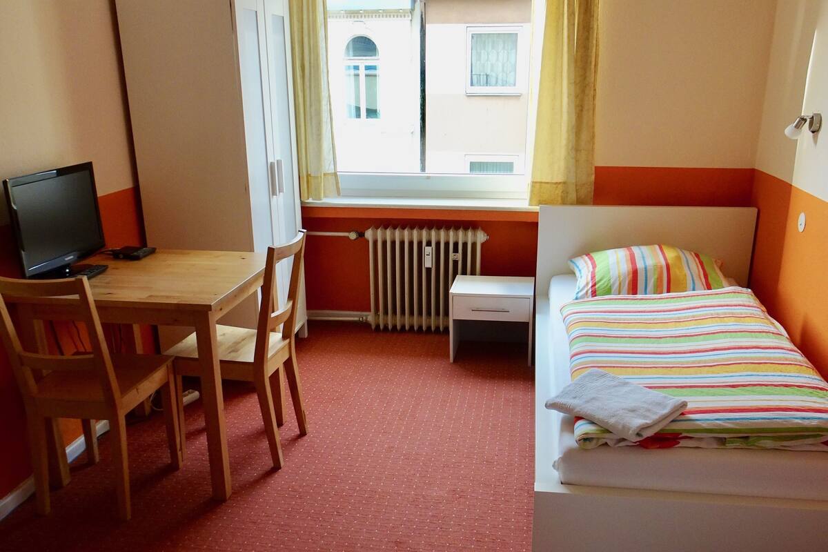 A hotel room with a desk, computer, two beds, and a window with curtains.