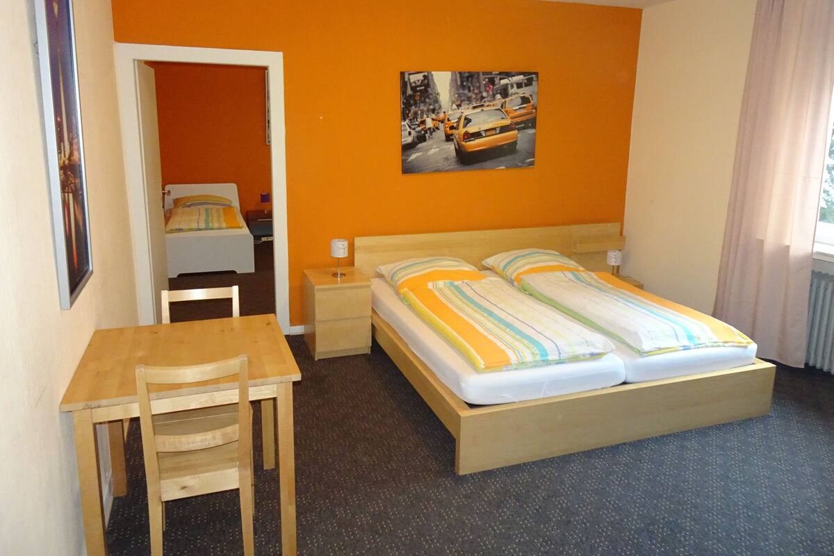 A hotel room with a bed, a desk, a chair, a nightstand, and a picture on the wall.