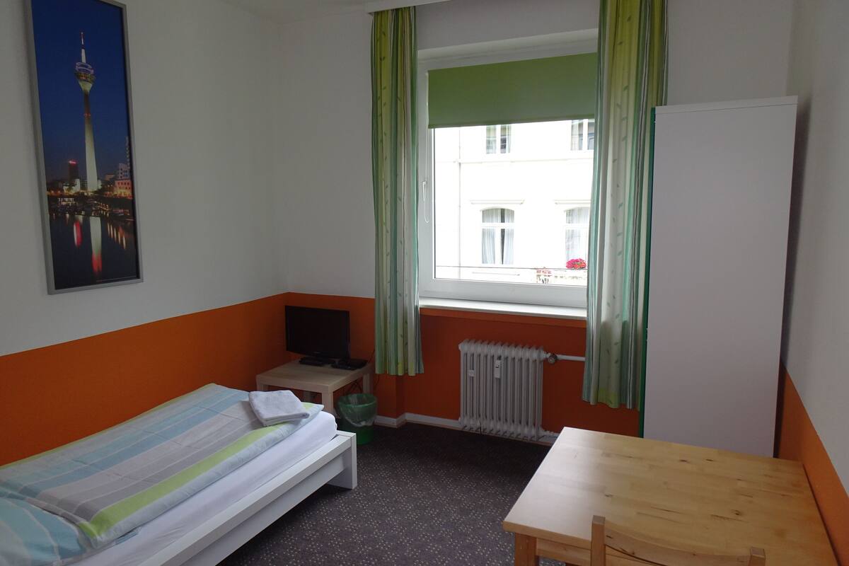 A room with a bed, a small table, a TV, and a window with curtains.