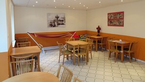 Un área de comedor con suelo de patrón hexagonal, mesas y sillas de madera, una hamaca y decoración en las paredes.