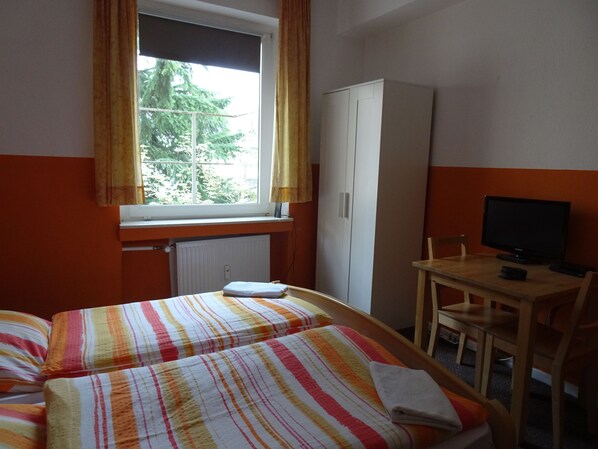 A bedroom with two beds, a desk, a chair, a television, and a wardrobe.