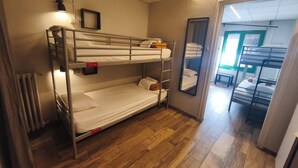 A bunk bed room with a wooden floor, a small table, and a mirror on the wall. - The Buba House - Hostel (Barcelona)