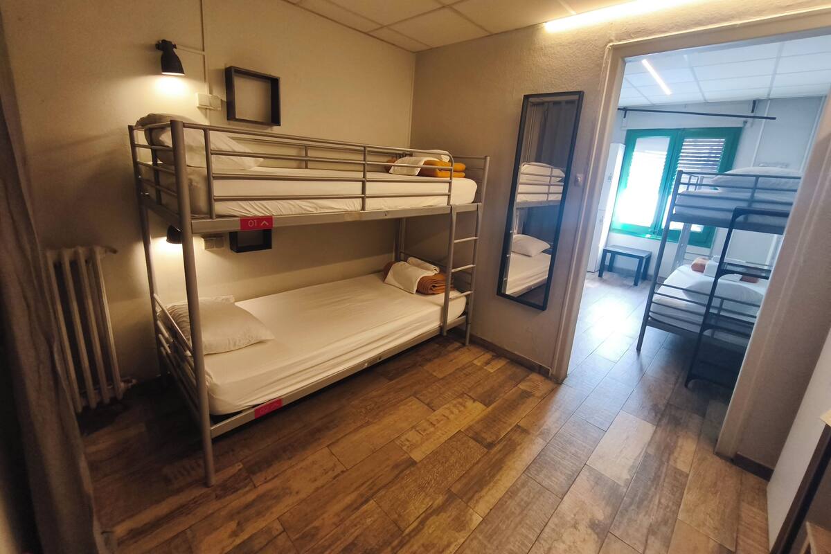 A bunk bed room with a wooden floor, a small table, and a mirror on the wall.