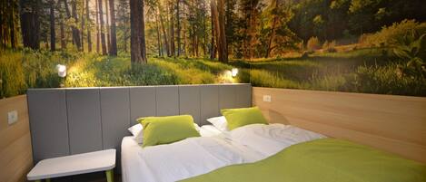 Une chambre à coucher avec un lit, deux tables de chevet et une fresque représentant une scène de forêt.