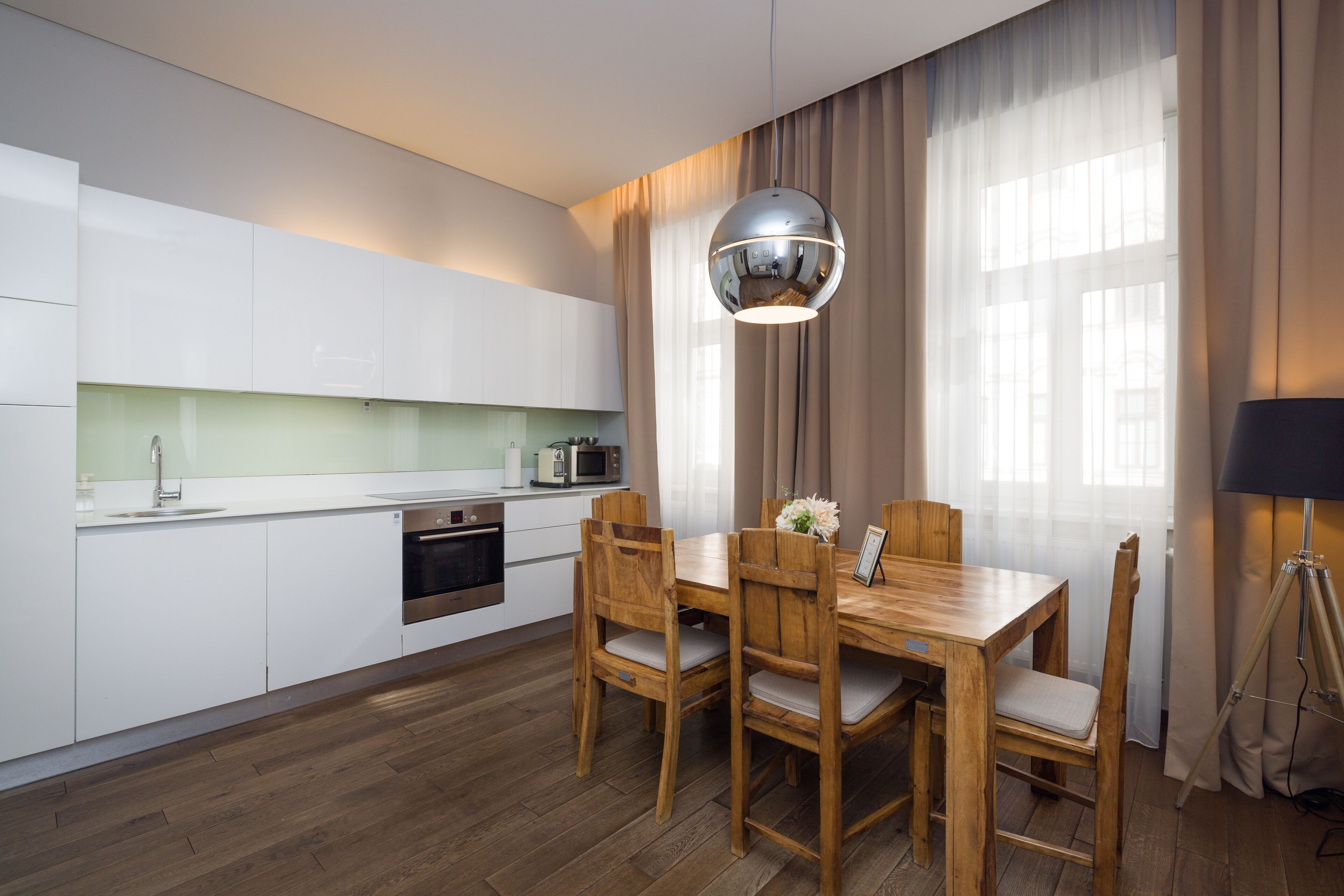 A modern kitchen with white cabinets, a wooden dining table, and a pendant light.