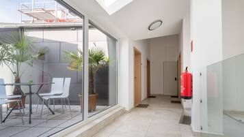 A modern interior with a glass wall overlooking a terrace, a fire extinguisher mounted on the wall, and a clean, tiled floor.