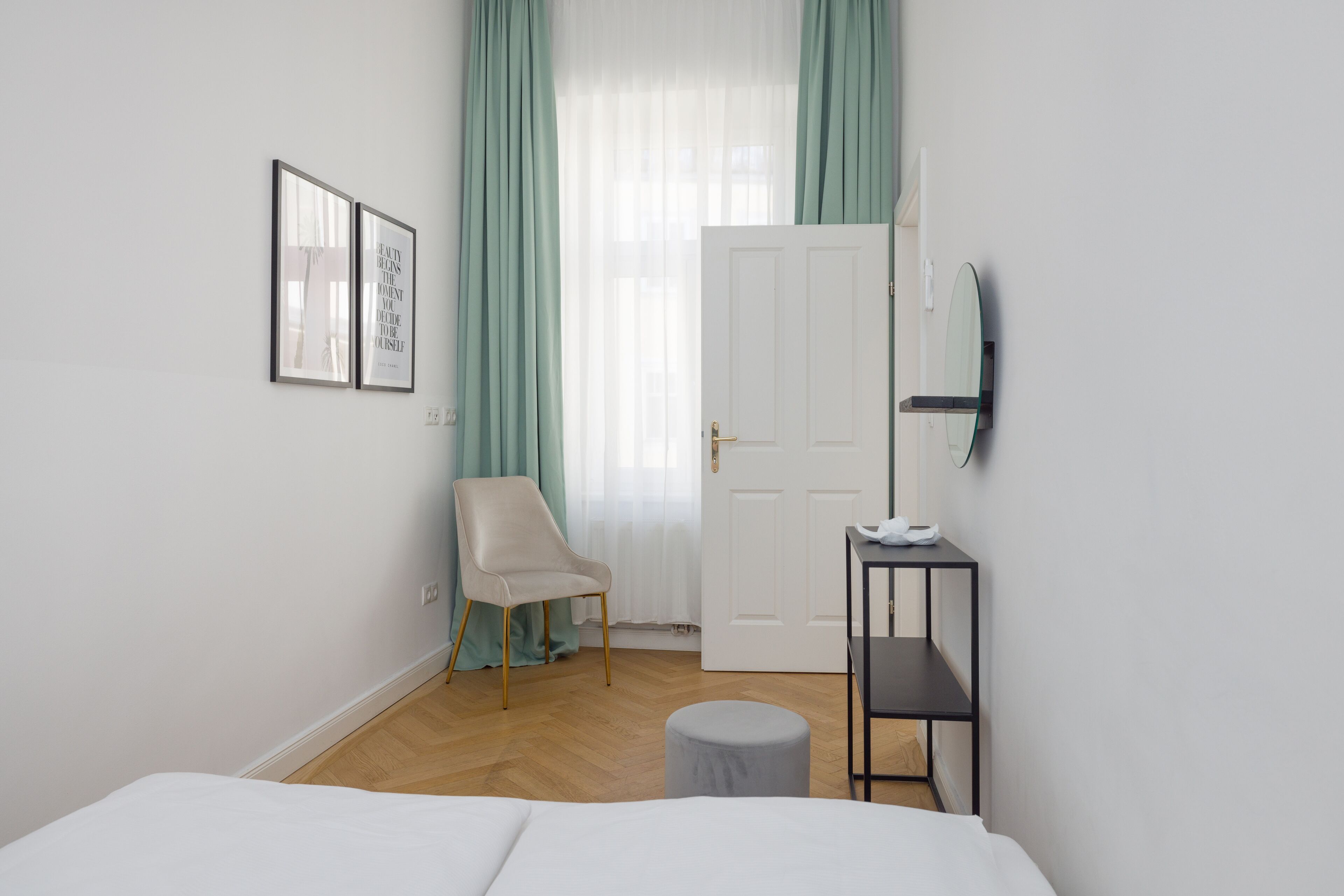 Ein schlicht eingerichtetes Schlafzimmer mit Bett, Stuhl, kleinem Tisch und Spiegel an der Wand.