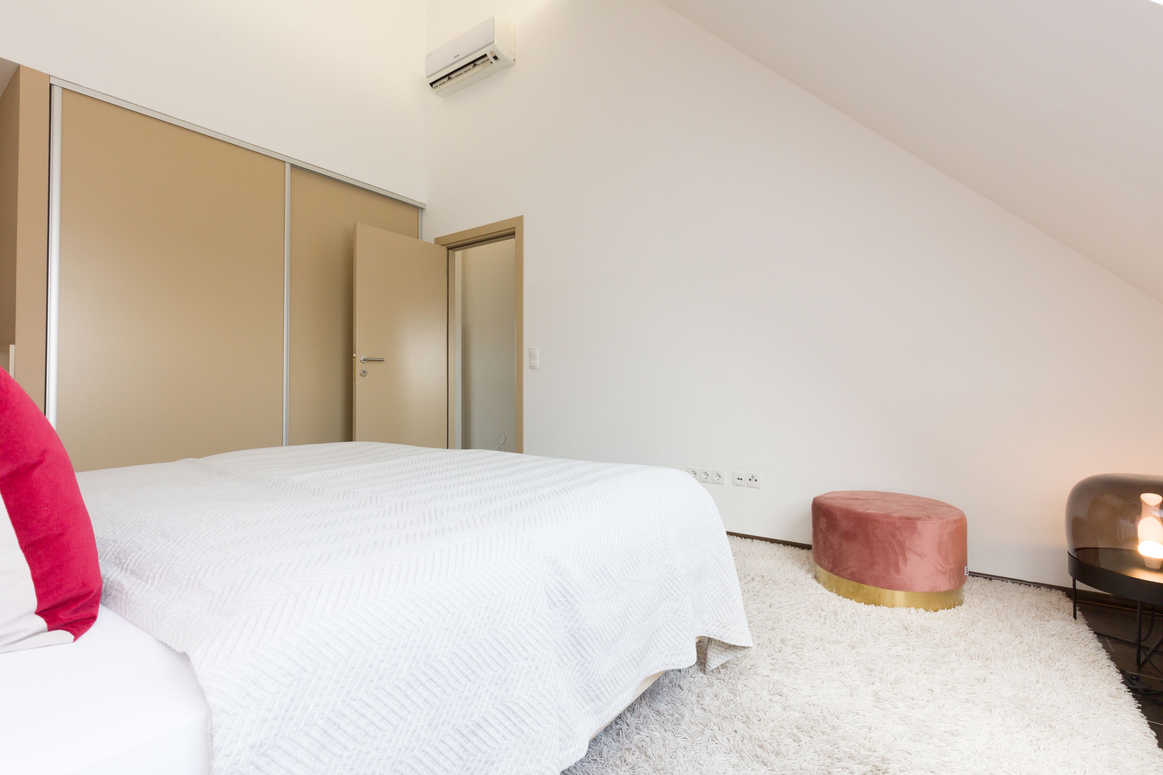 Una camera da letto con un letto, un armadio, un poggiapiedi rotondo e un comodino.