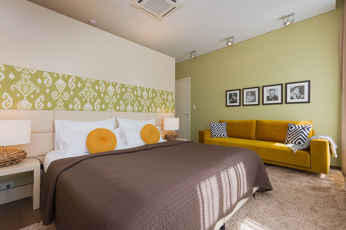 A hotel room with a large bed, a yellow sofa, and a wall with framed pictures.