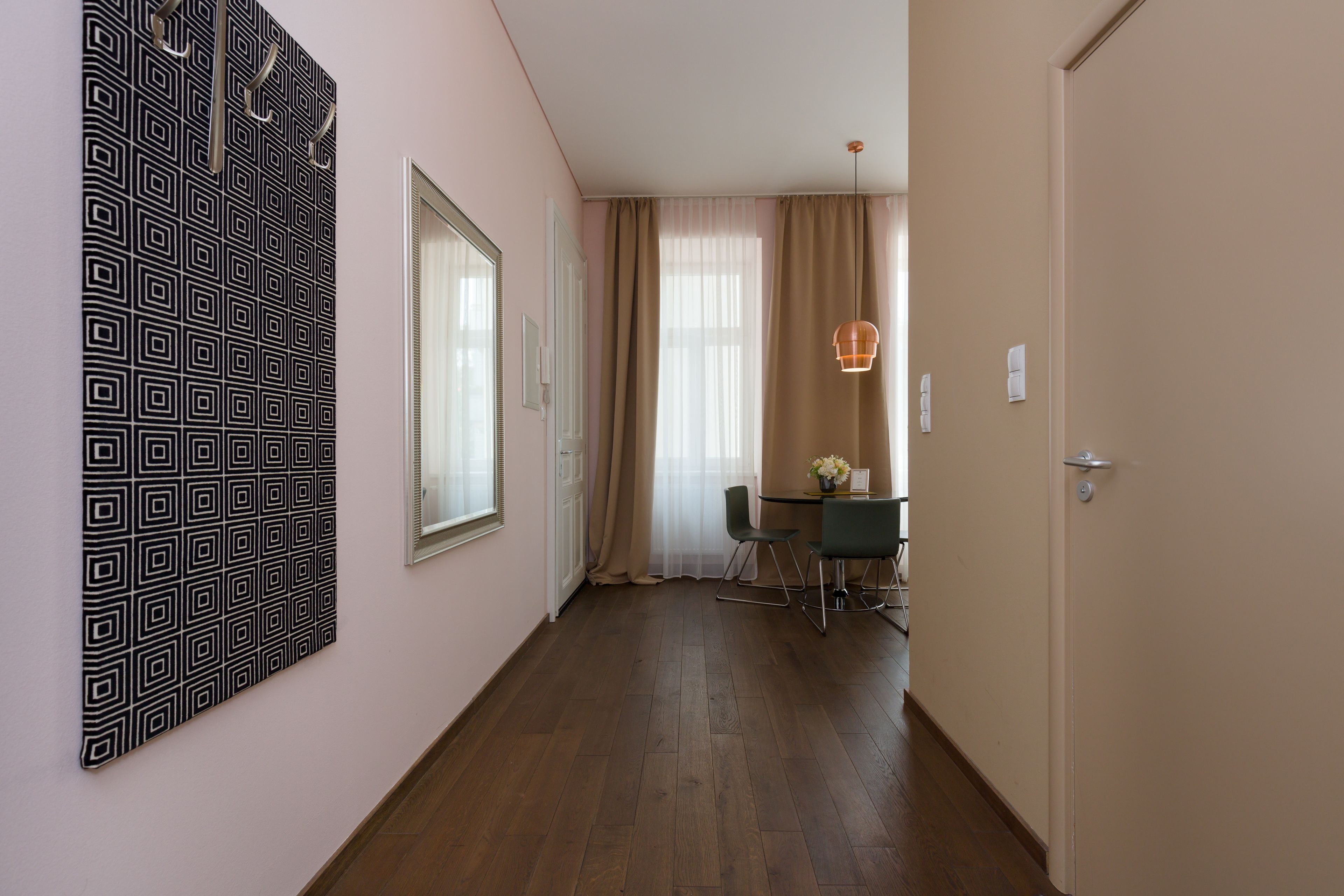 Un pasillo con un papel tapiz decorativo, un comedor con mesa y sillas, y una puerta a la derecha.