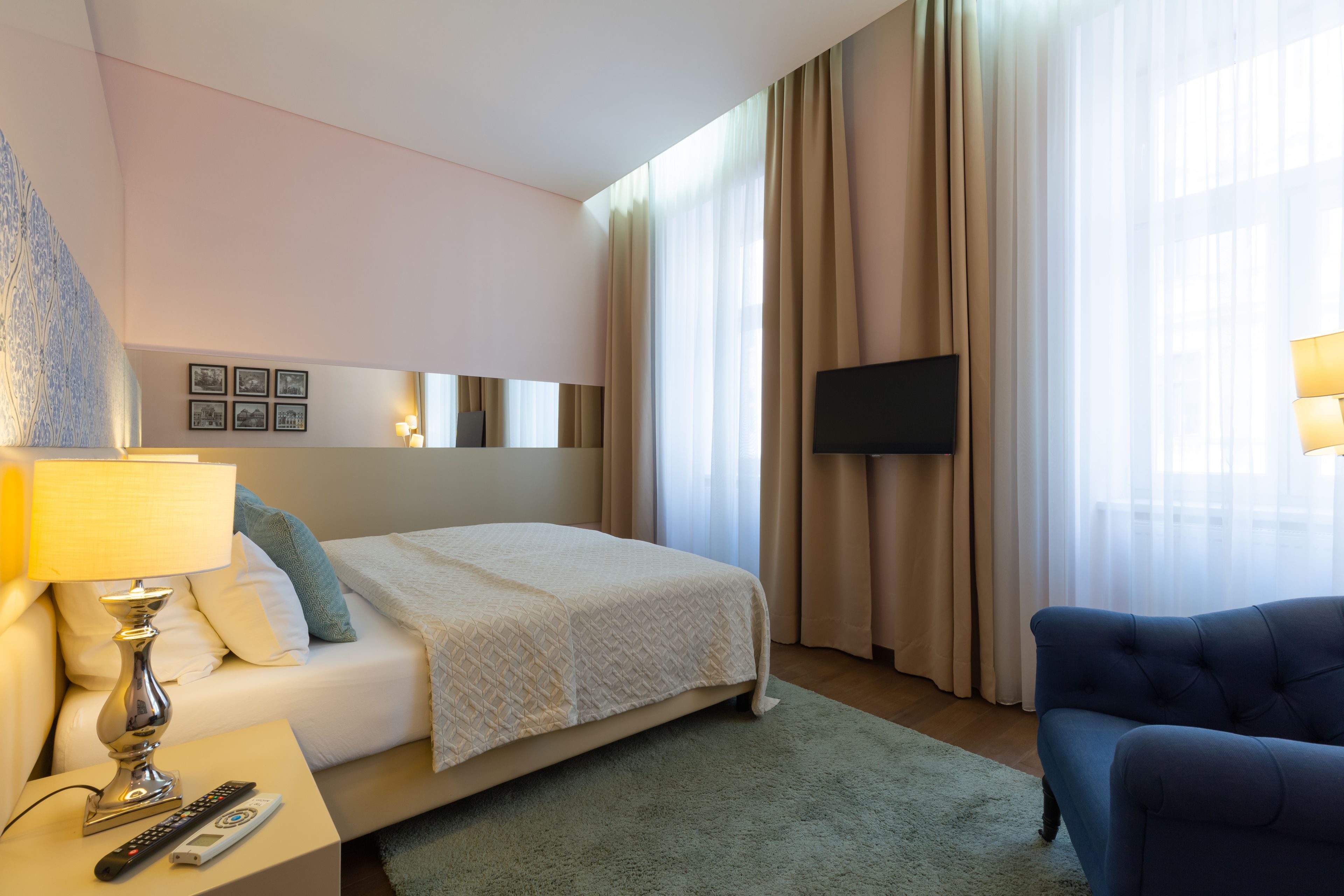 Habitación de hotel con cama, televisor, lámpara, control remoto y un sillón azul.