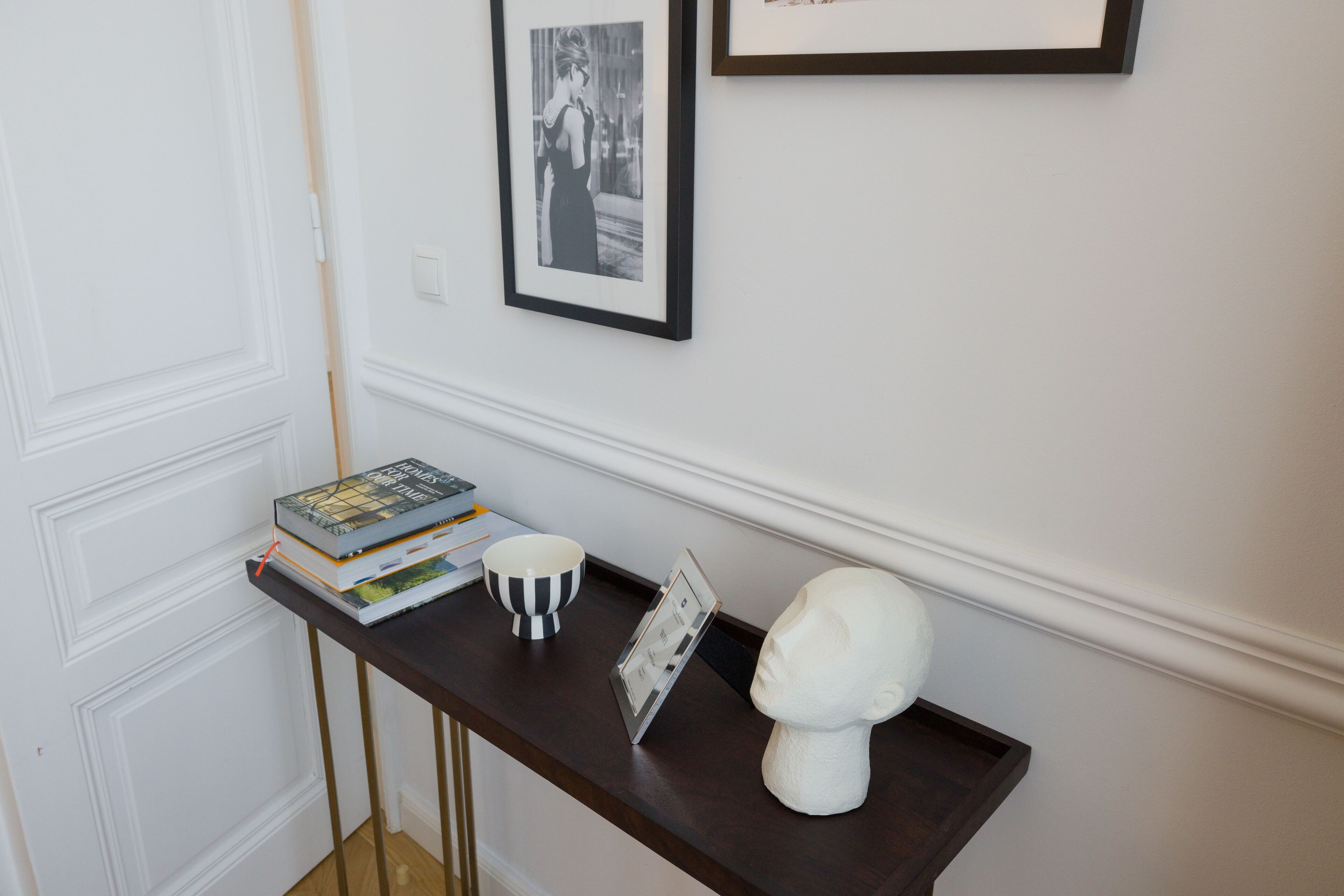 A dark wooden console table with a white bust, a framed photo, a bowl, and books.