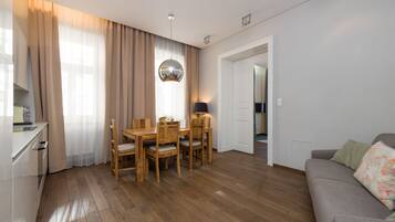 Een moderne woonkamer met een houten eettafel, stoelen, een grijze bank en een keuken met een wit aanrecht en kastjes.