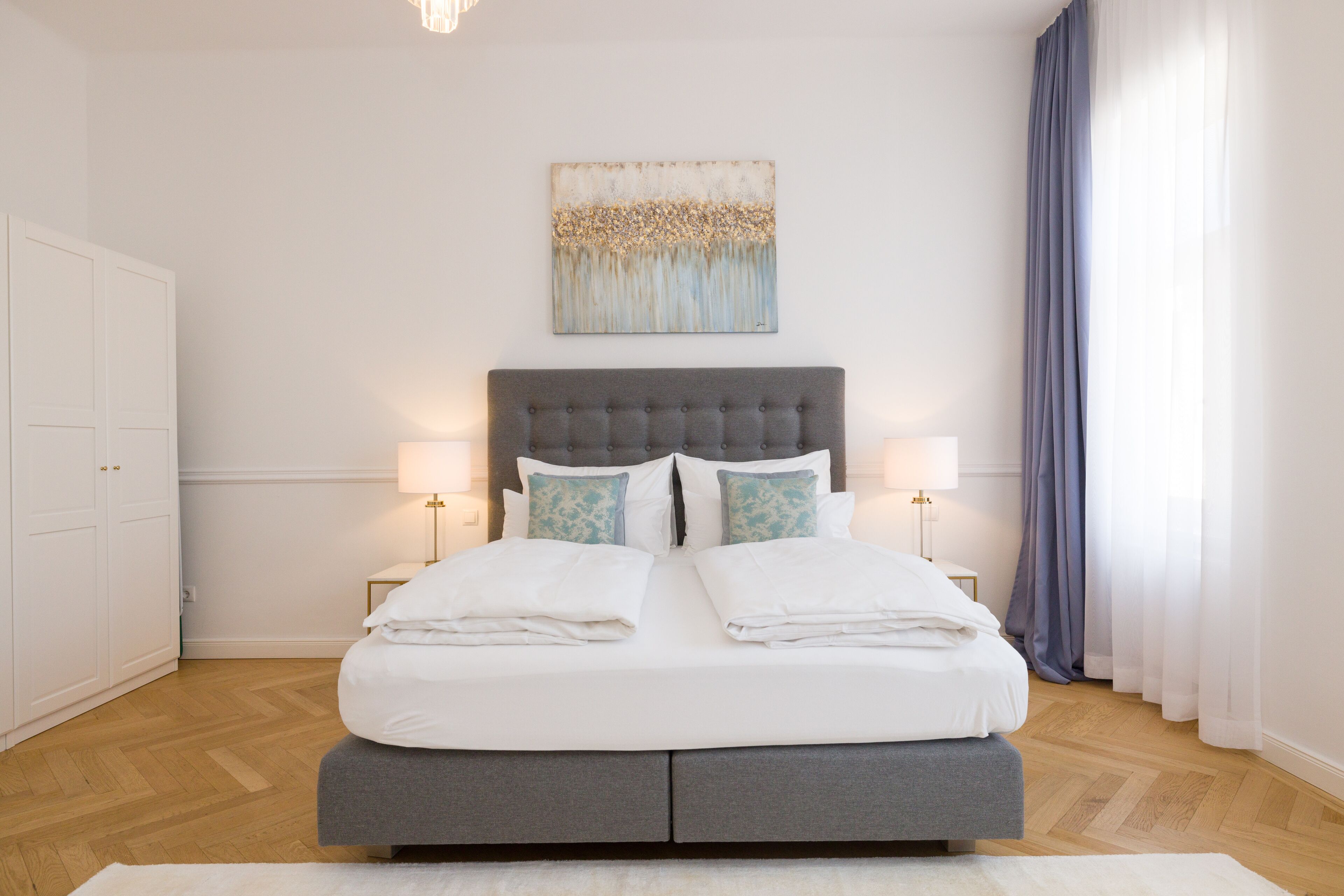 Quarto com uma cama grande, duas mesas de cabeceira, uma cabeceira, um quadro na parede e uma janela com cortinas.