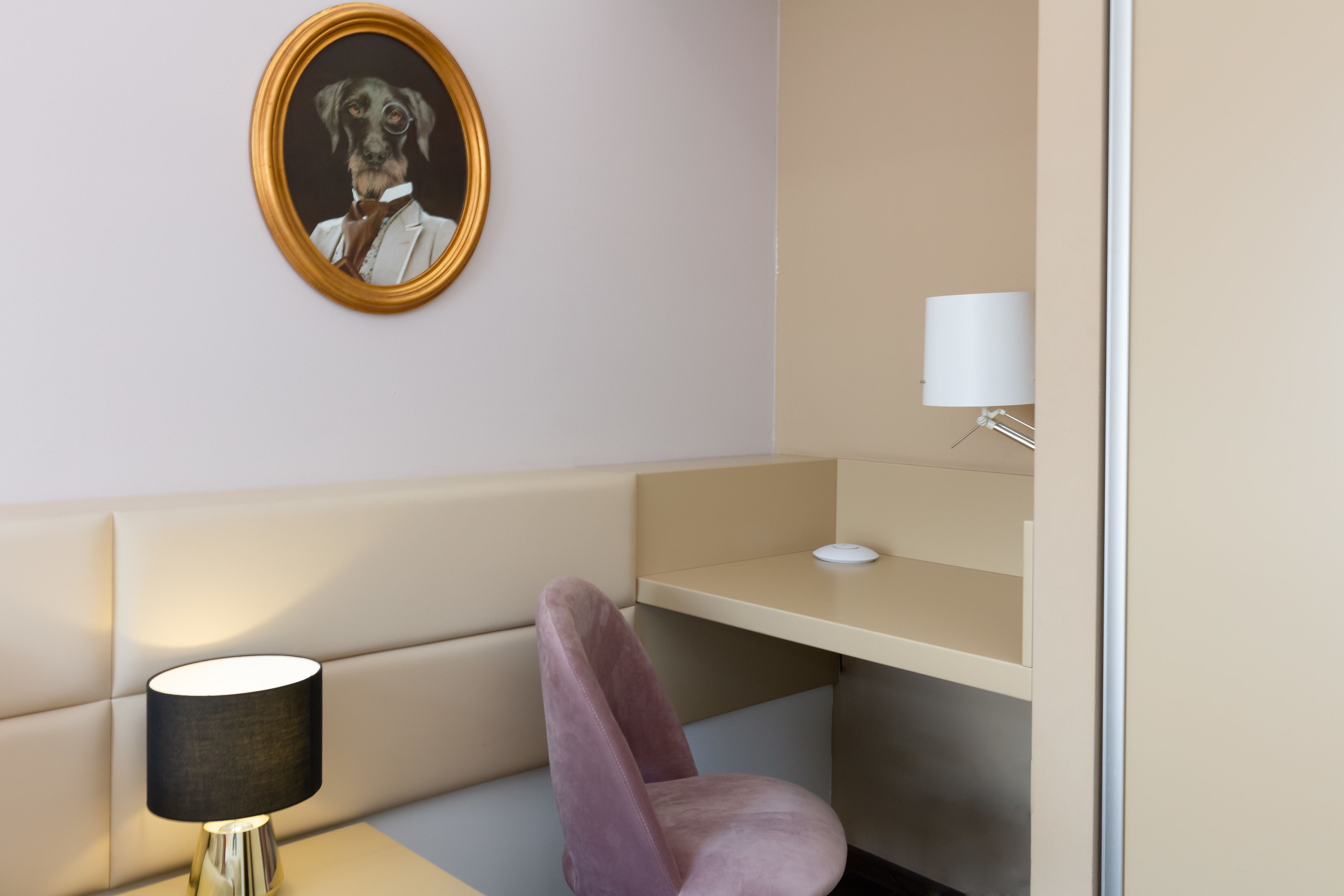 A modern room with a beige sofa, a desk, a lamp, and a framed portrait on the wall.