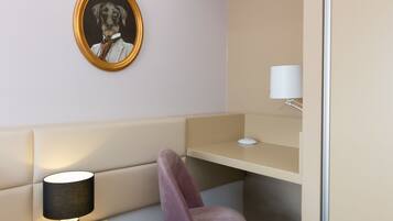 A modern room with a beige sofa, a desk, a lamp, and a framed portrait on the wall.