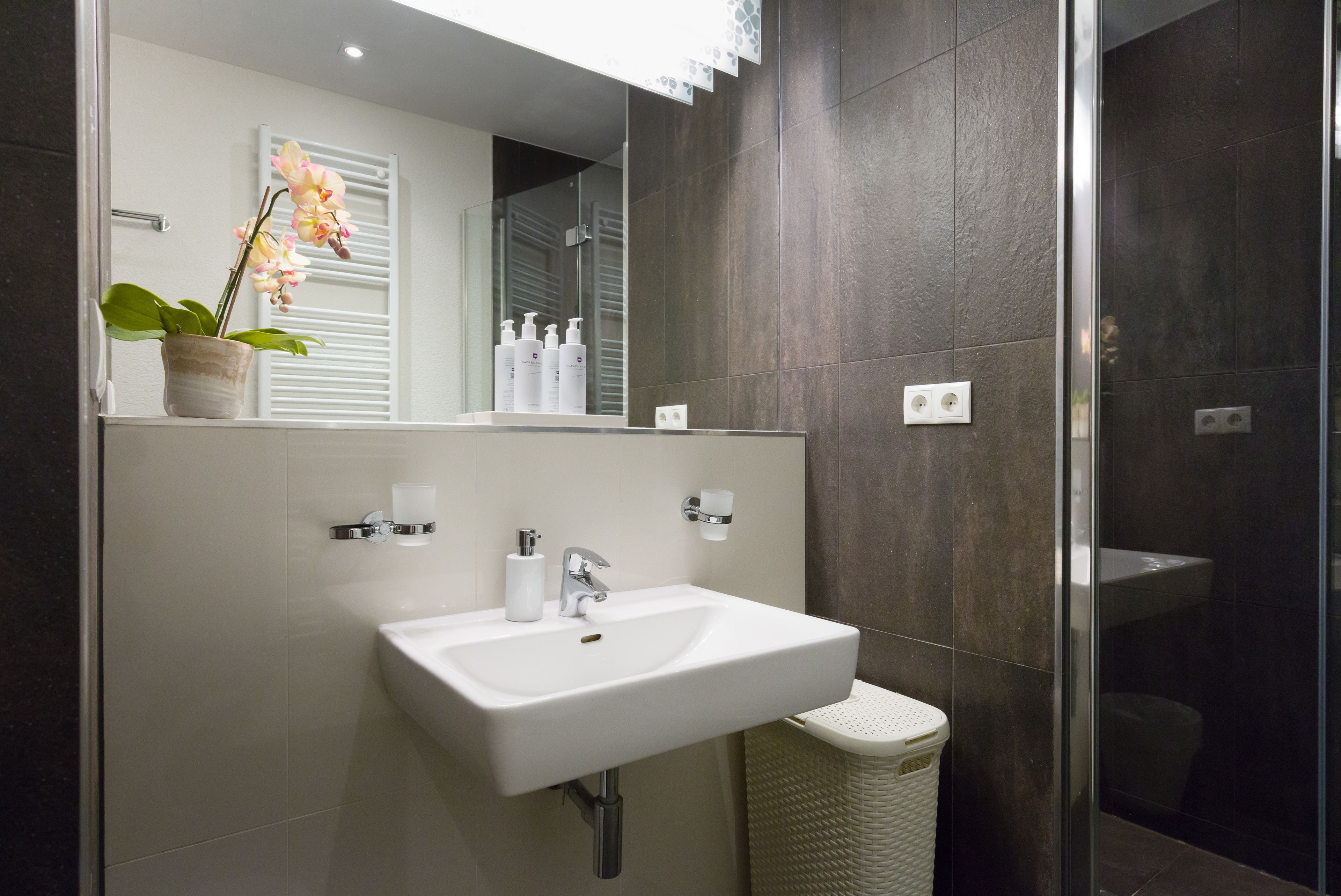 Ein modernes Badezimmer mit einem weißen Waschbecken, einem Spiegel und einer Topforchidee.