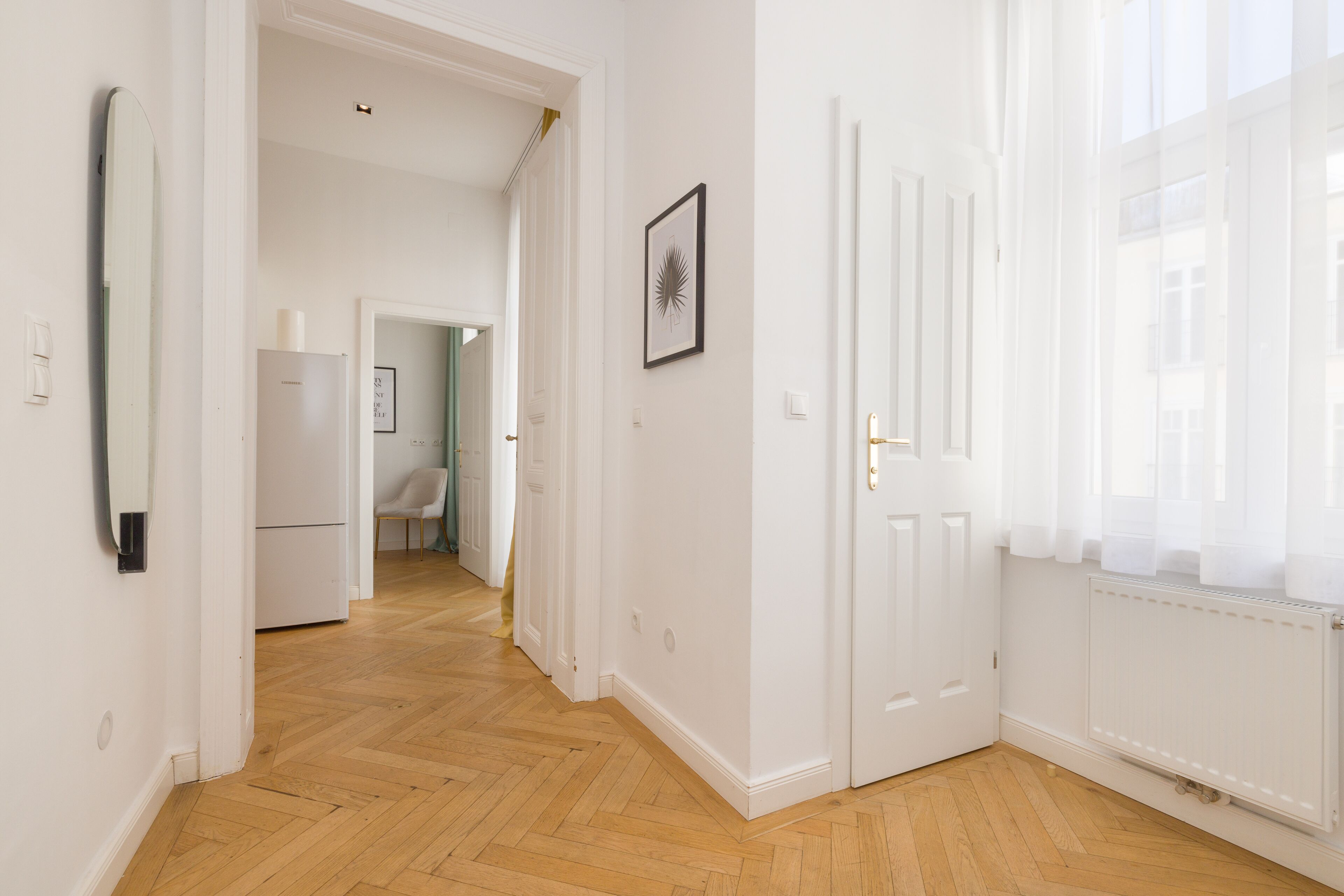 A hallway with wooden flooring, white walls, and a door leading to another room.