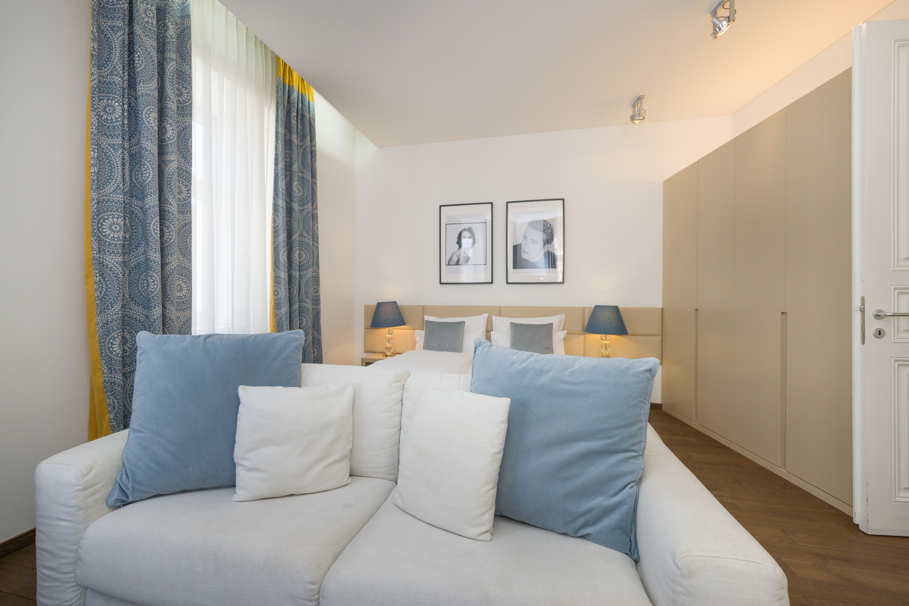 A modern hotel room with a white sofa, two framed pictures on the wall, and a wardrobe.