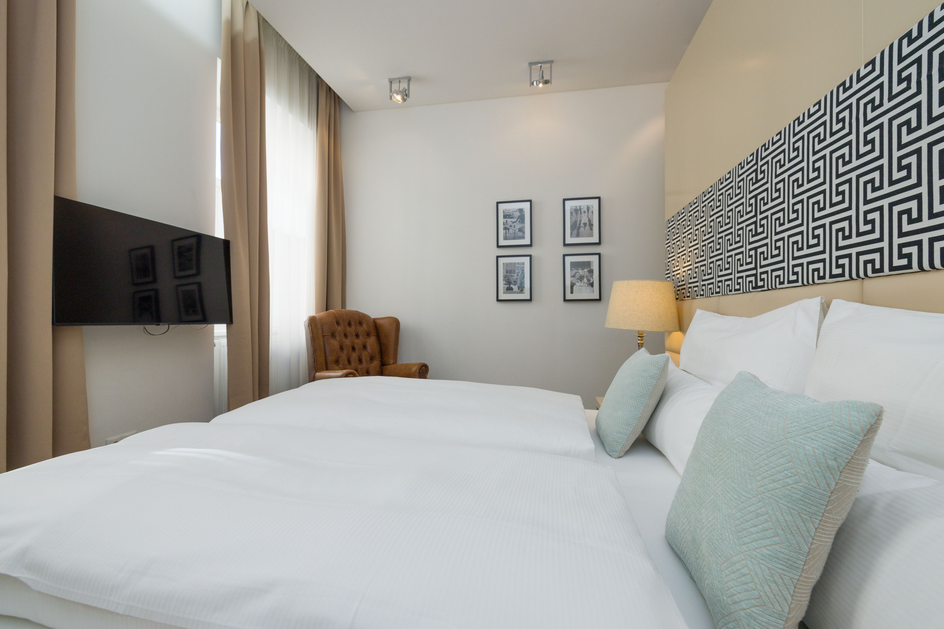 A hotel room with a large bed, a flat-screen TV mounted on the wall, a chair, and a wall with framed pictures.