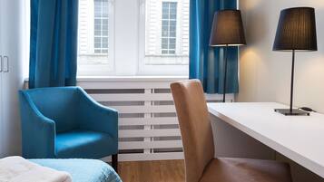 Ein Hotelzimmer mit einem Bett, zwei Stühlen, einem Schreibtisch und einem fenster mit Vorhängen.