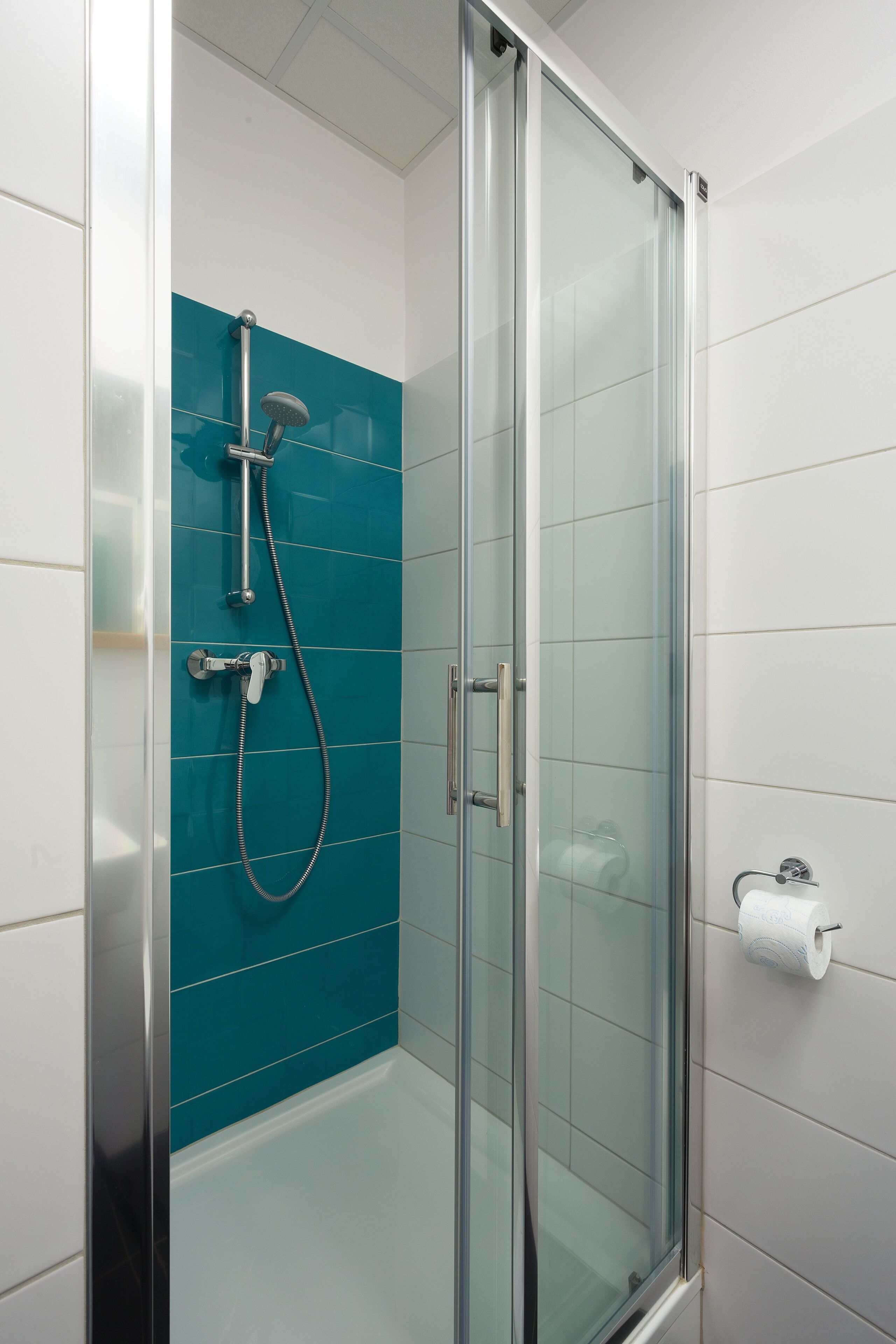 Una cabina de ducha con paredes de vidrio, un cabezal de ducha de mano y un grifo instalado en la pared.