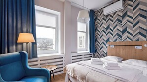 Una habitación de hotel con una cama, un sillón azul, una mesita y una ventana con cortinas.