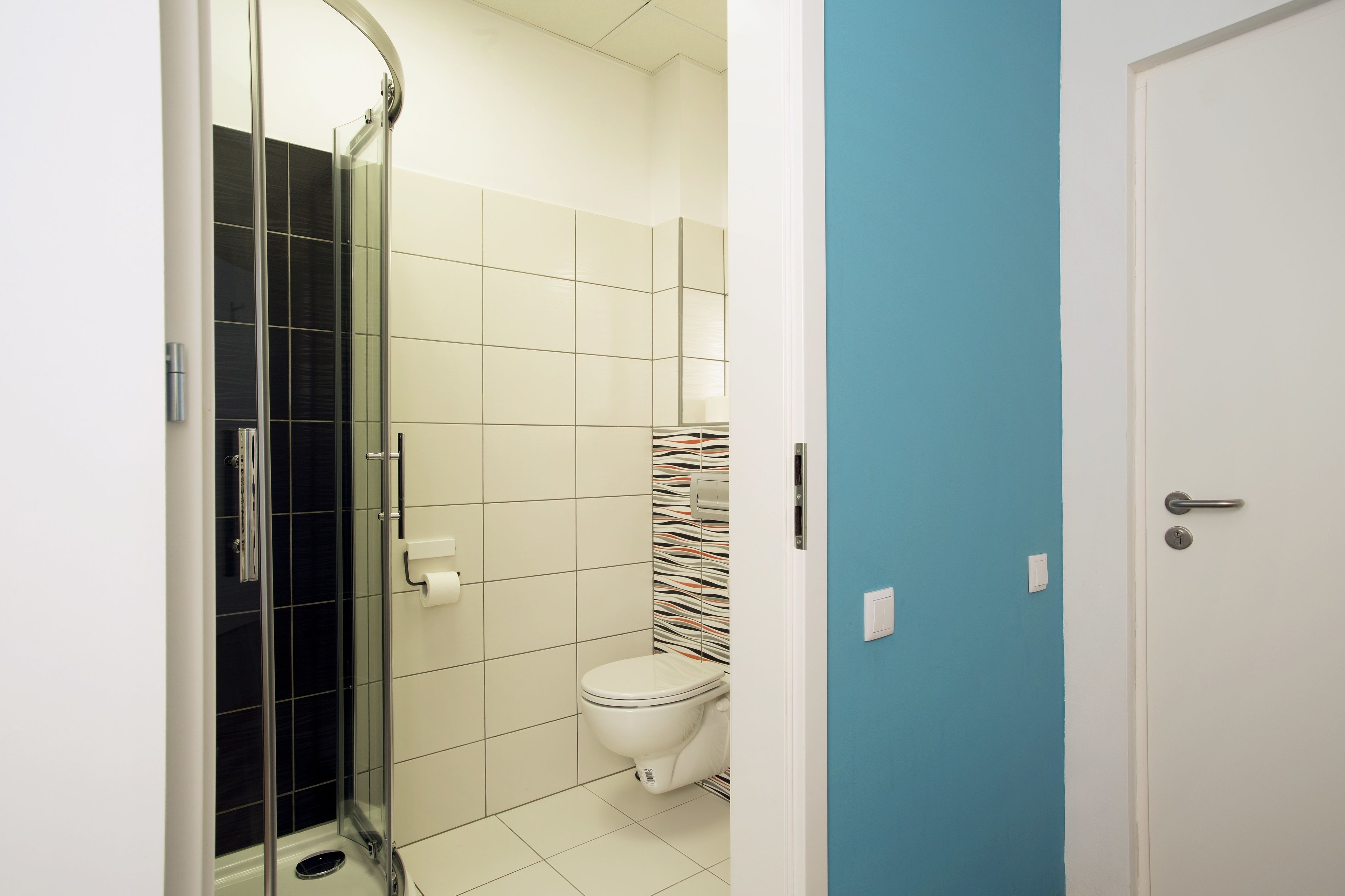 Une salle de bain avec une douche à parois de verre, des toilettes blanches et un mur d’accent bleu.