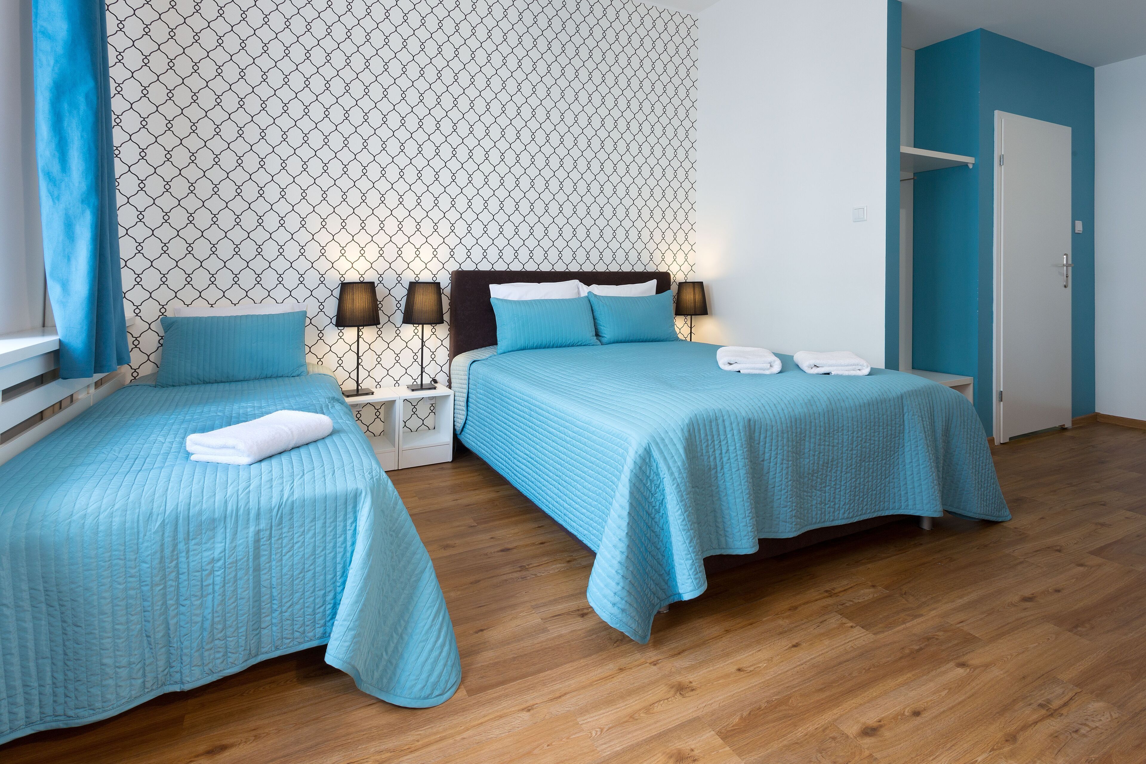Habitación de hotel con dos camas, un papel tapiz estampado y suelo de madera.