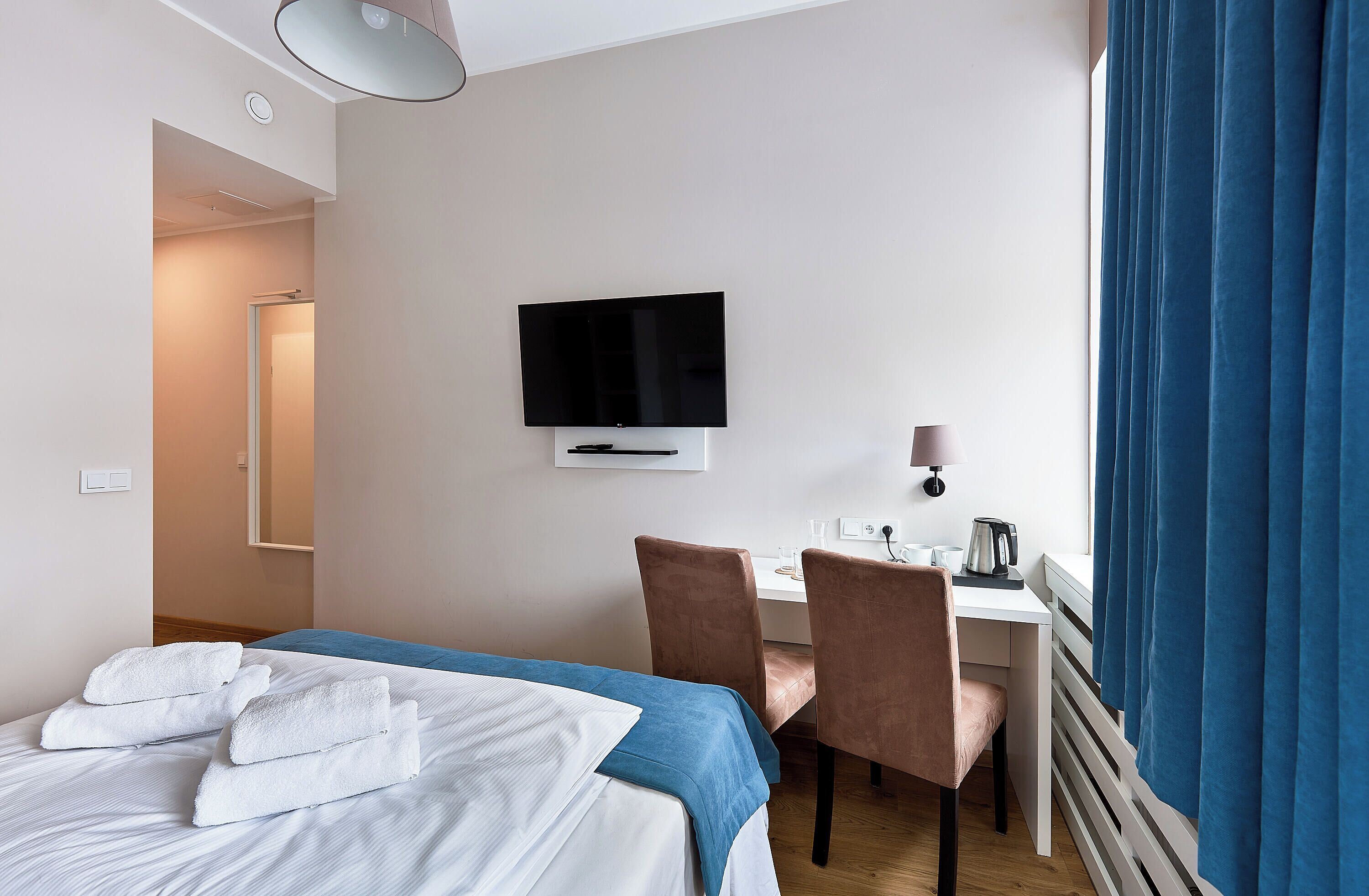 Ein Hotelzimmer mit Bett, Schreibtisch, Stuhl, Fernseher und einem Fenster mit Vorhängen.